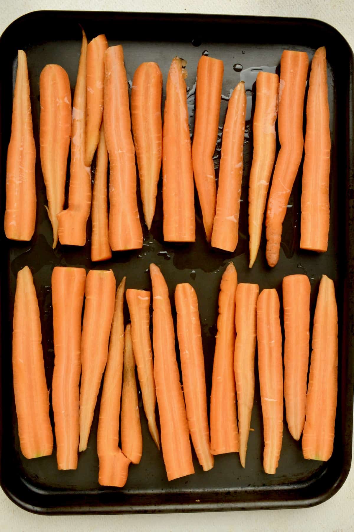 Halved carrots on a roasting tray.