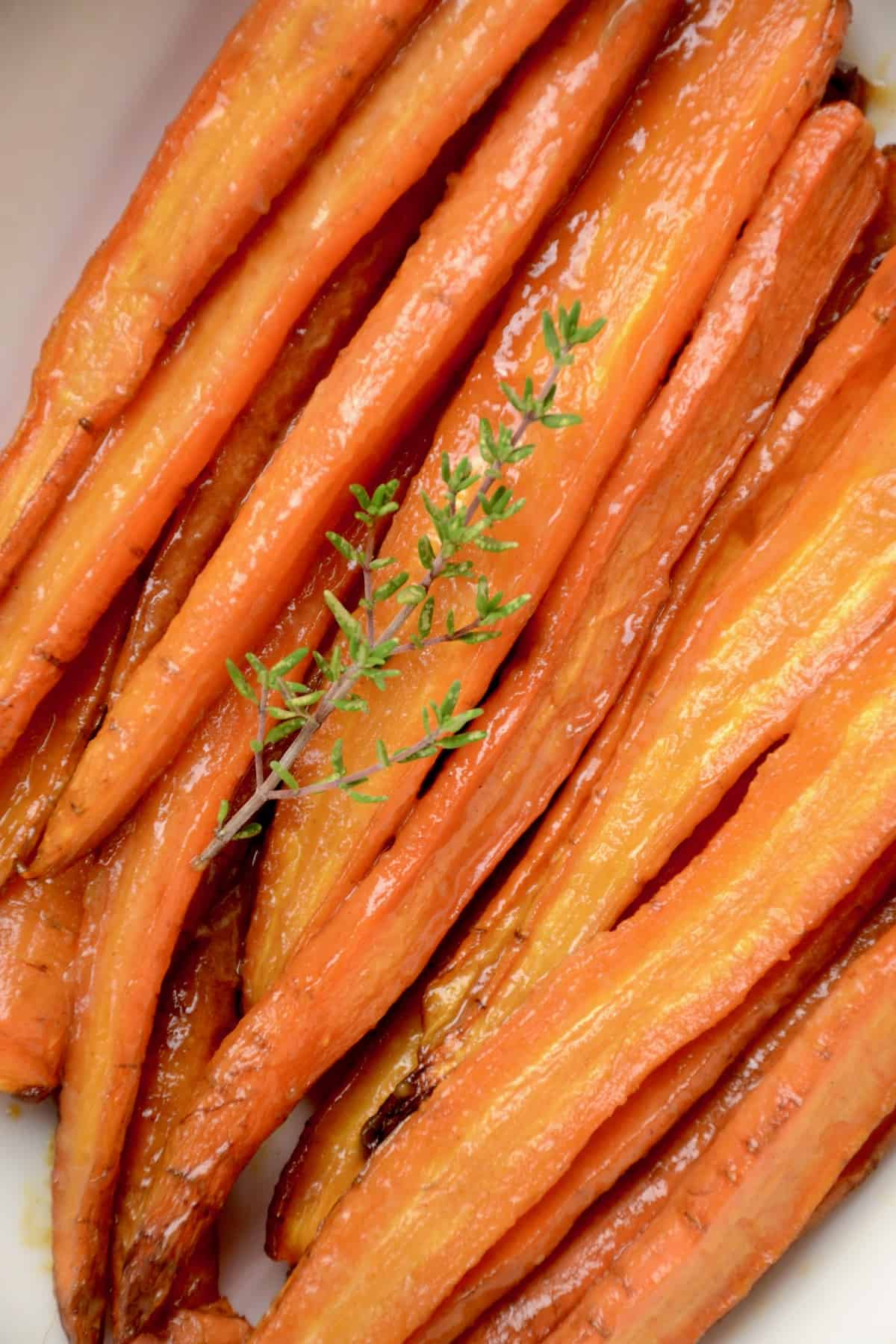 Glazed carrots in a serving dish with a twig of fresh thyme.