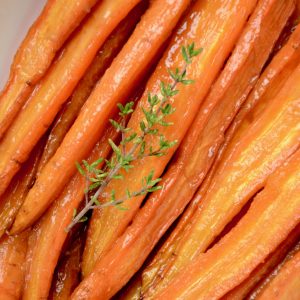 Glazed, roasted carrots and a twig of fresh thyme in a serving dish..