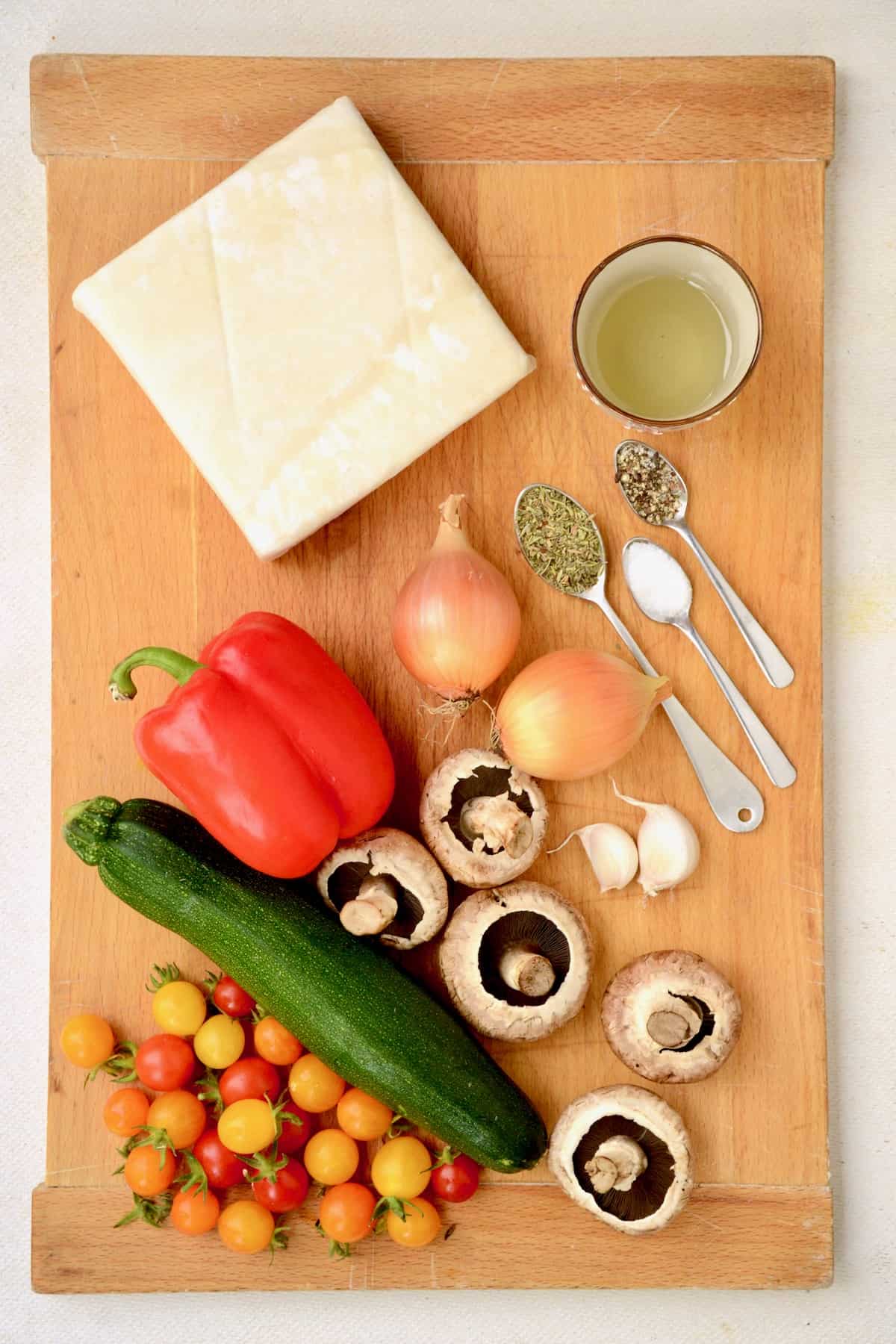 A block of puff pastry, seasonings and vegetables on a wooden board.