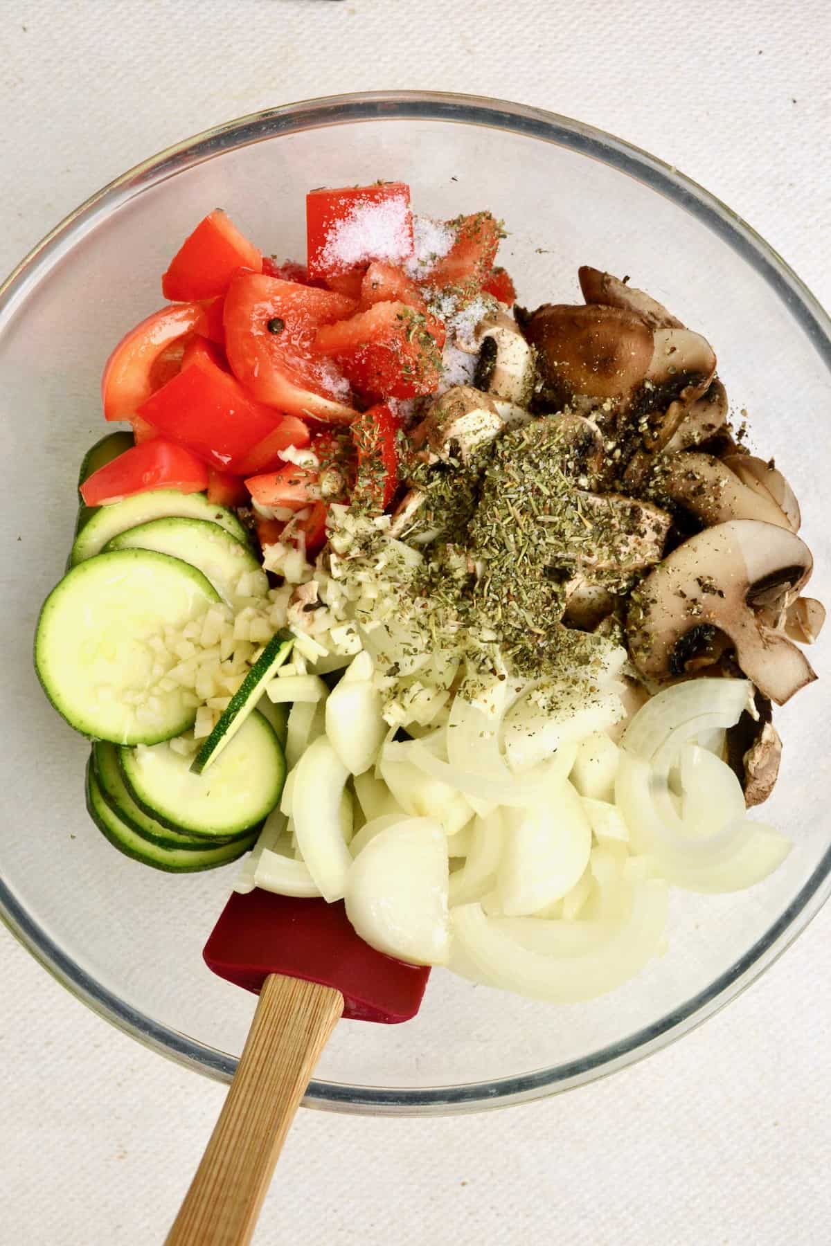 Zucchini, pepper, mushroom, onion and onion slices in a bowl with dried herbs.