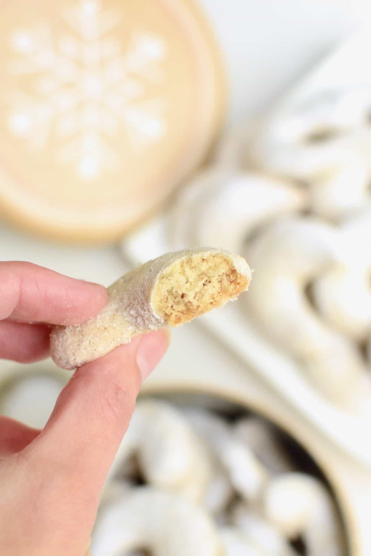 A half vanilla crescent cookie is held up towards the camera to reveal its crumbly and light inner texture.