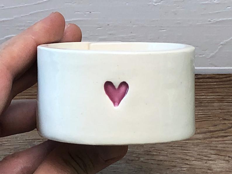 A handmade white ceramic bowl decorated with a small heart shape.