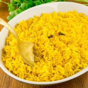A brass spoon dips into the serving bowl of yellow rice.