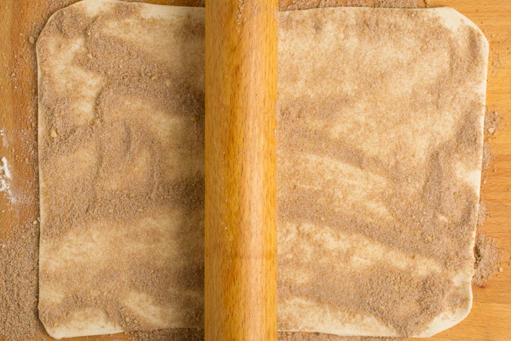 A rolling pin gently presses the sugar into the pastry.