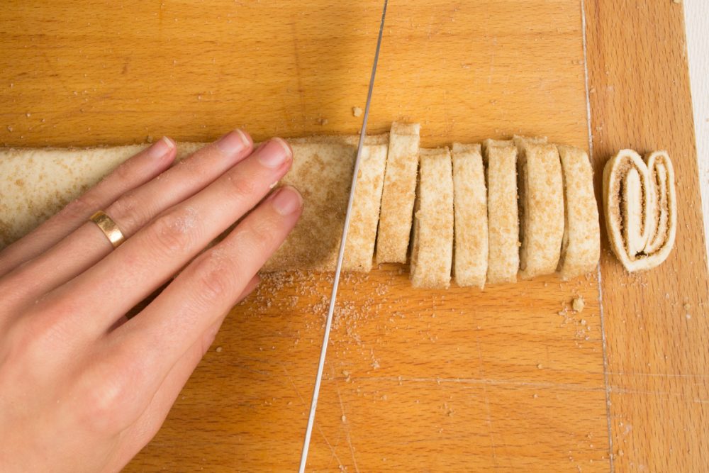 A knife cuts the pastry strip into slices, revealing their folded pattern inside.