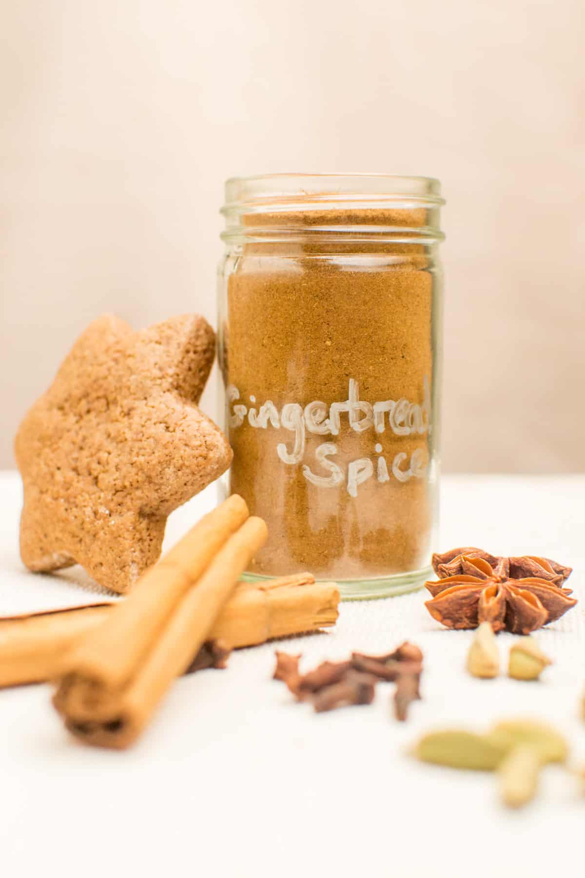 A small jar of spices next to a gingerbread cookie and whole spices.
