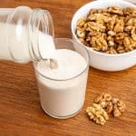 Pouring the milk into a glass, next to a bowl of walnut halves.