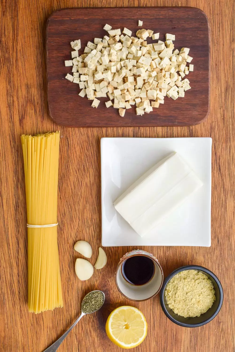 Ingredients for the vegan carbonara - a block of silken tofu, diced smoked tofu, a bunch of spaghetti, garlic cloves, herbs, half a lemon, soy sauce and nutritional yeast.