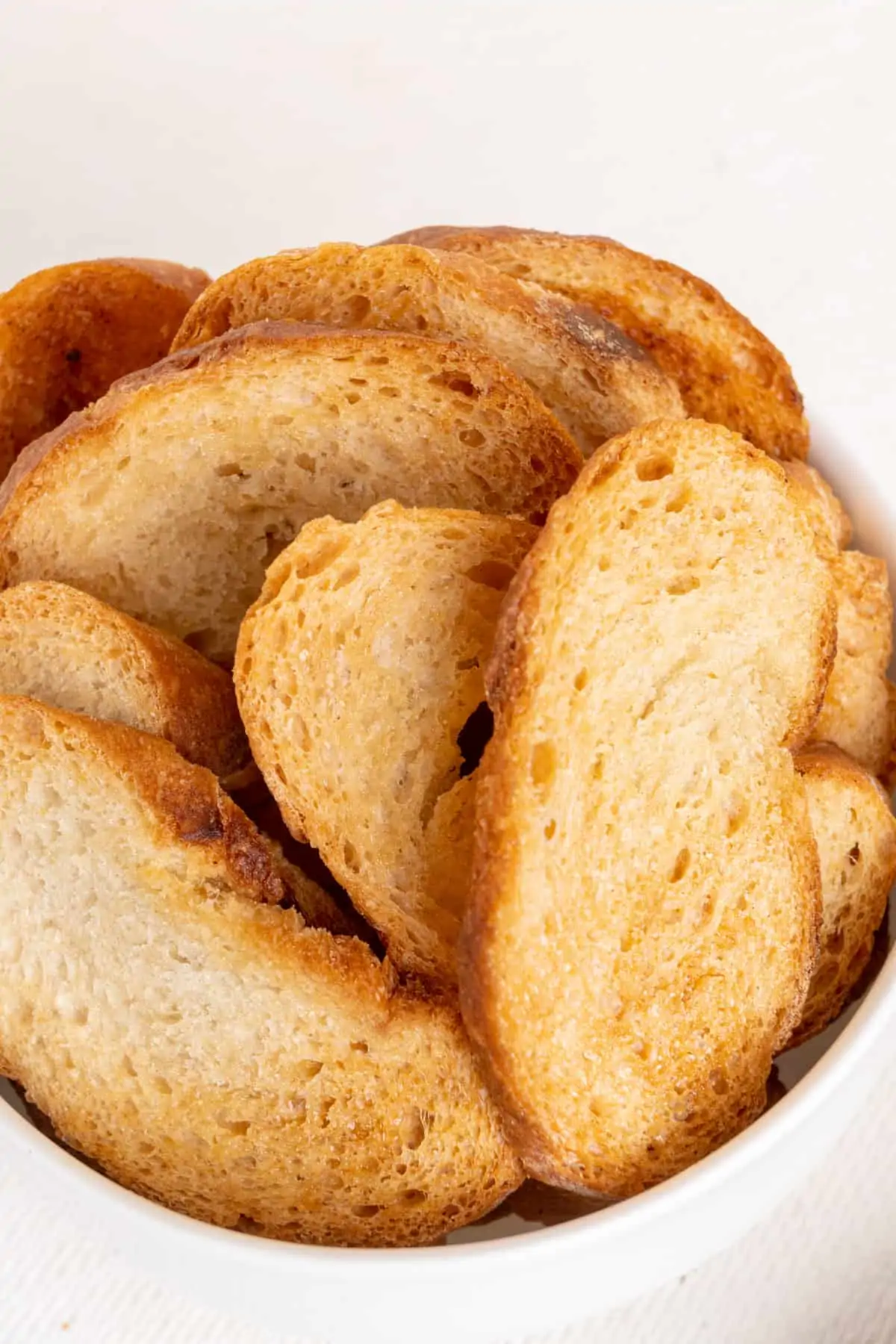A bowl of thin slices of baguette, baked golden brown and crispy.