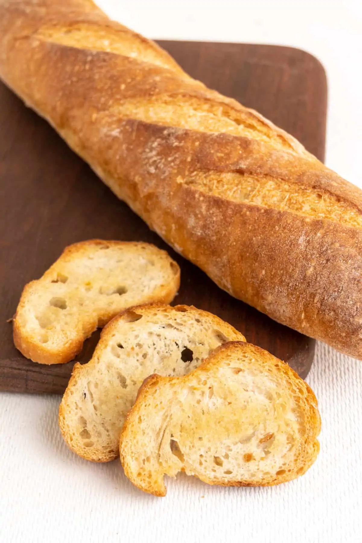 Three crostini, which are crispy baked thin slices of bread, next to a baguette on a wooden board.