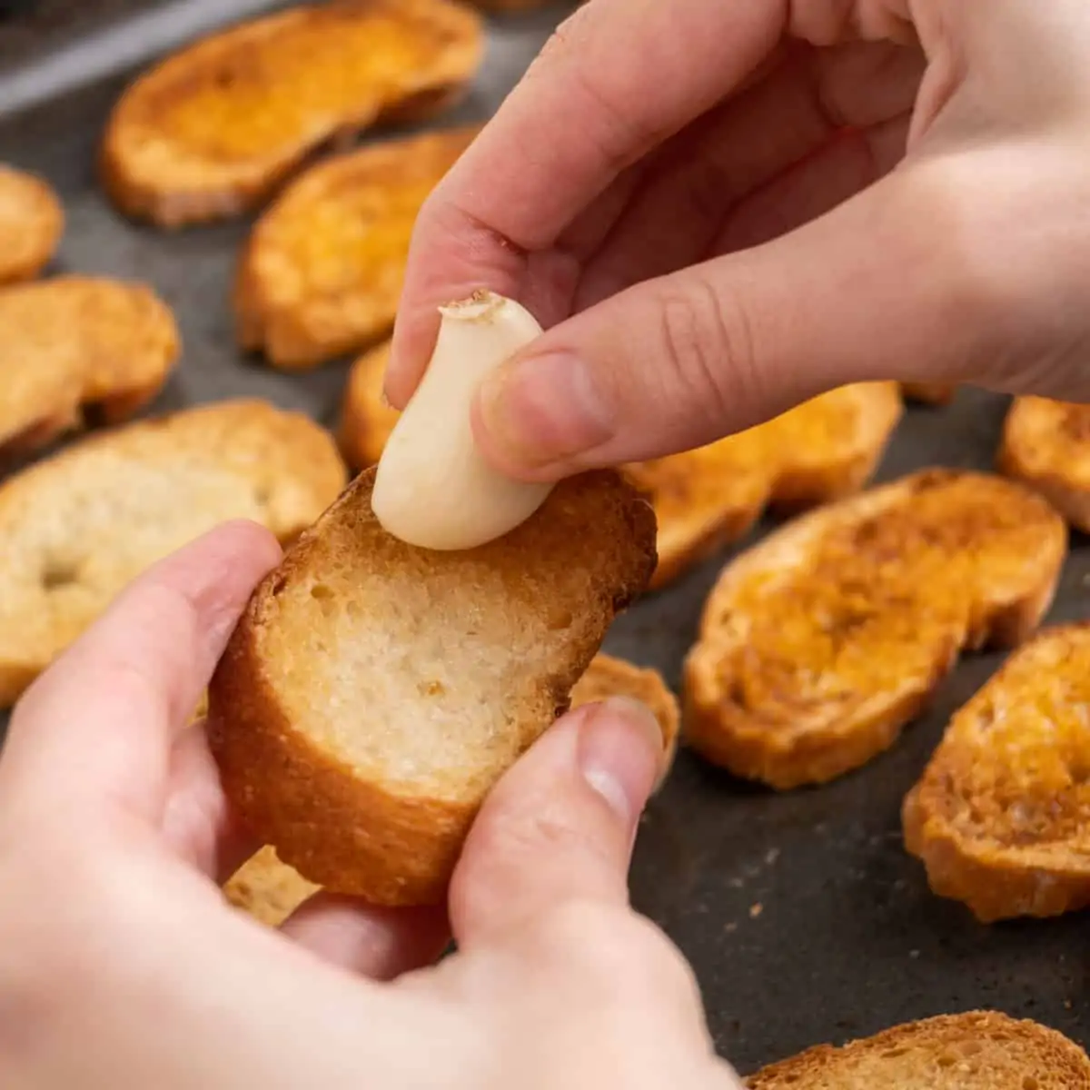 A fresh garlic clove is rubbed across a crostini to flavour it.