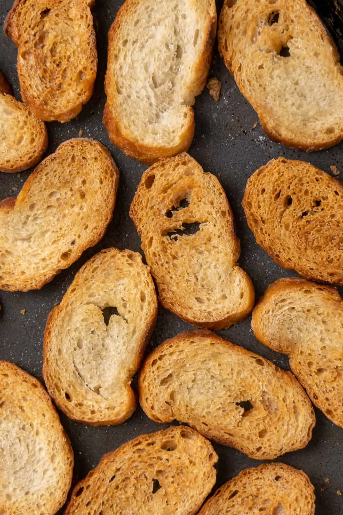 Small oval golden brown re-baked slices of bread on a baking tray.