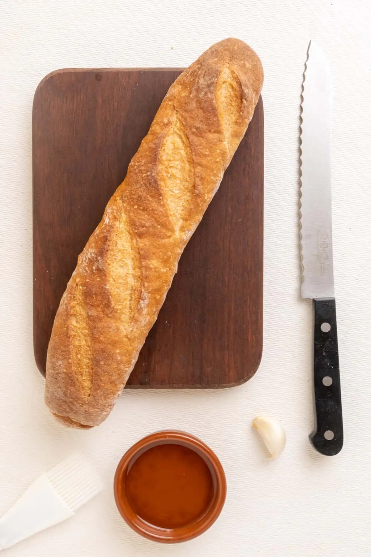 The ingredients for making crostini the traditional way: A long and thin white loaf of bread, some olive oil and a clove of garlic..