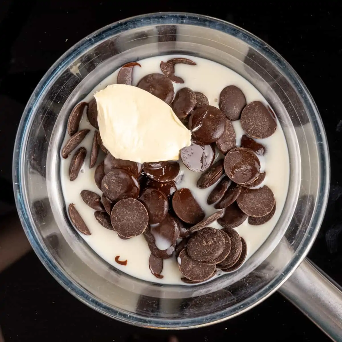 Chocolate buttons, oat milk, vegan butter, and maple syrup in a heatproof bowl over a pan.