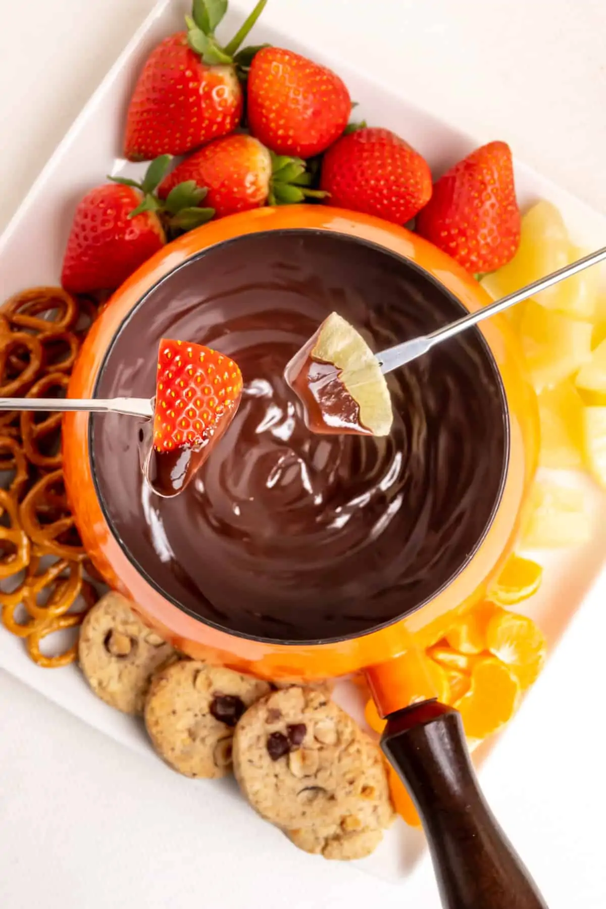 Dipping strawberry and pineapple into a pan of chocolate fondue.