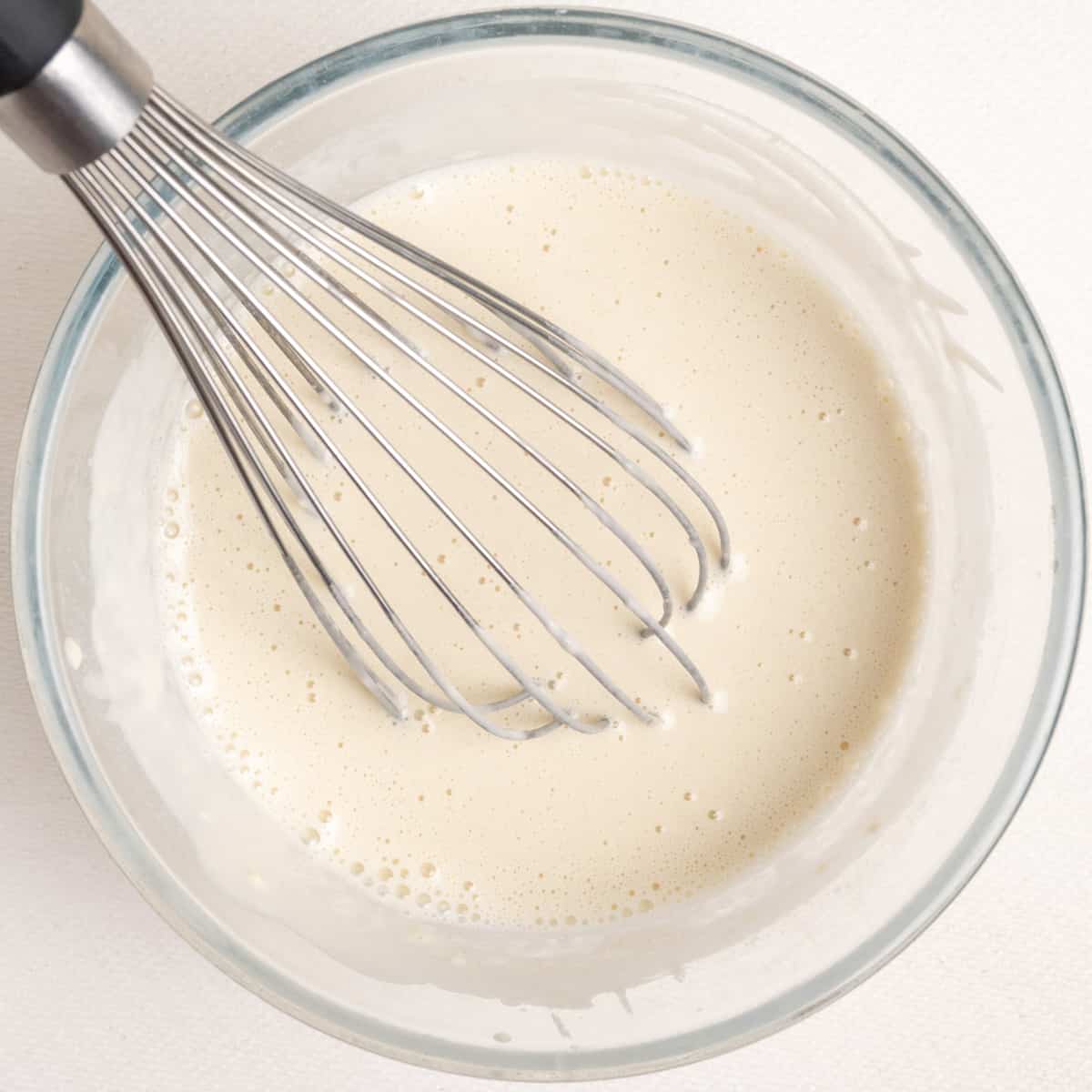 A smooth batter in a glass bowl with a whisk.