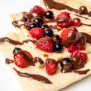 Three folded crepes on a plate topped with berries and chocolate sauce.