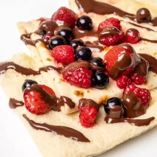Three folded crepes on a plate topped with berries and chocolate sauce.