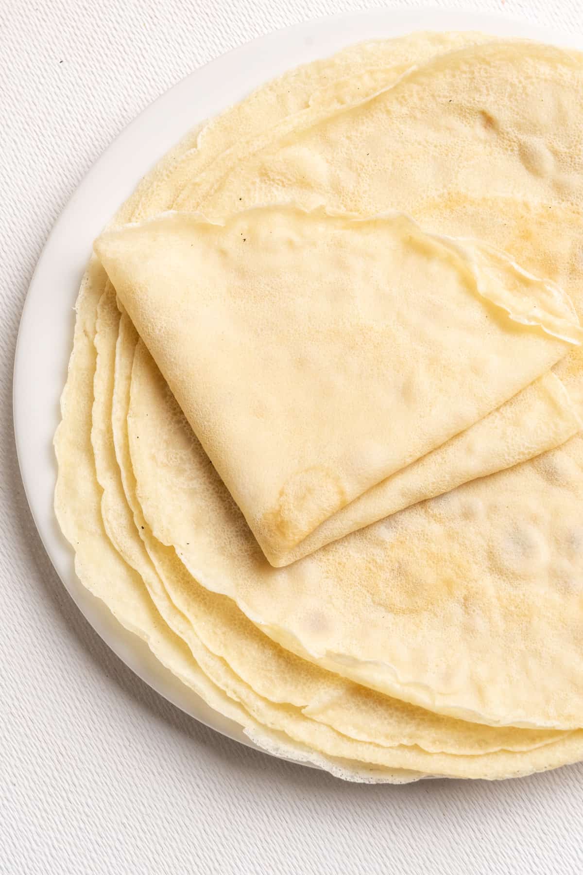 A stack of vegan crepes on a plate, the top one is folded into quarters.