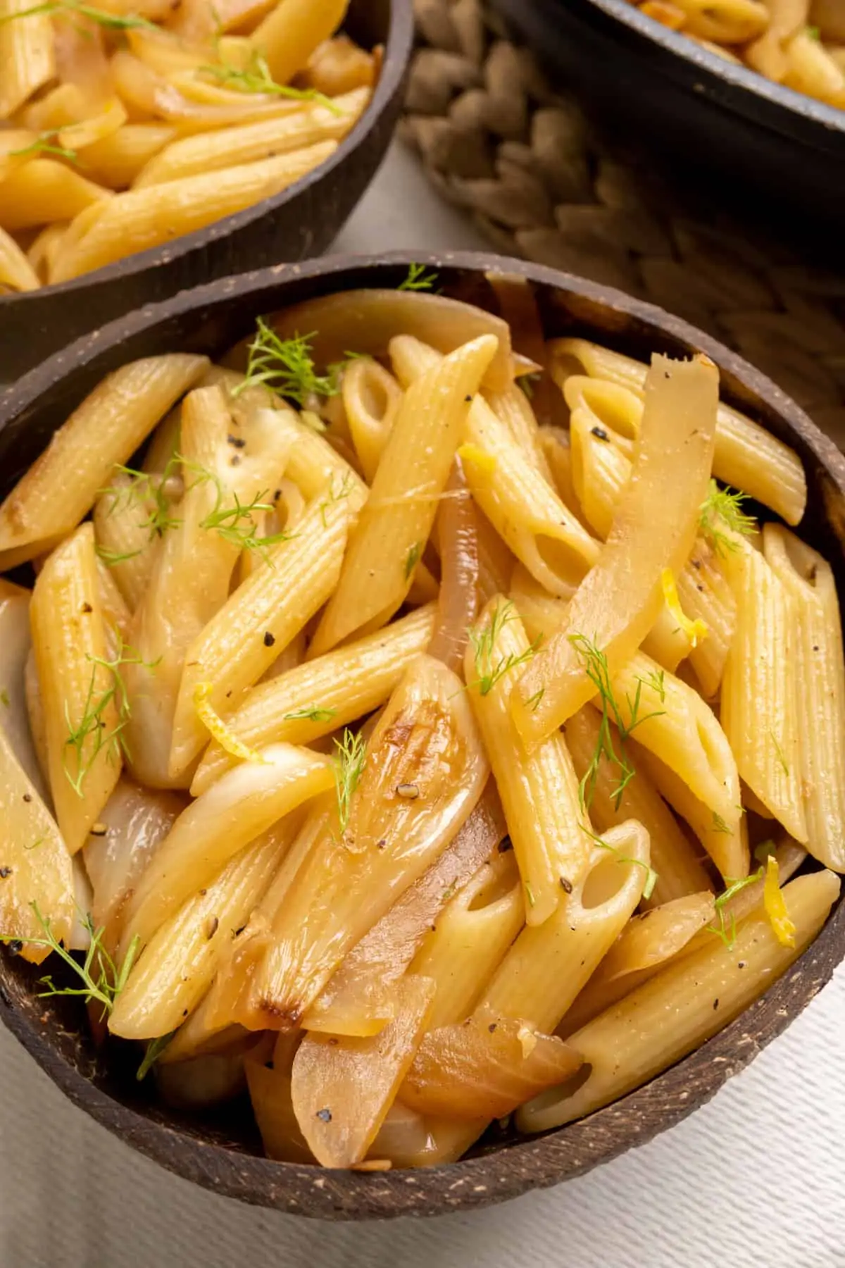 A portion of fennel pasta showing off the beautifully fried slices of fennel and onion and the garnish of green fennel fronds and some lemon peel.