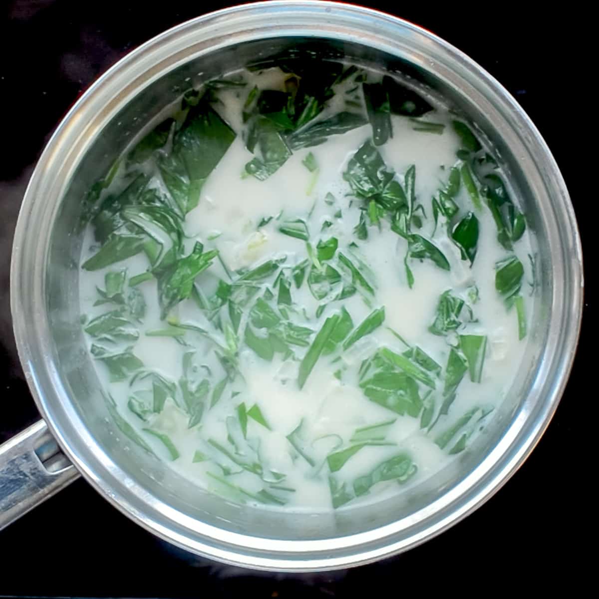 Chopped green leaves wilting down in the coconut and onion broth.