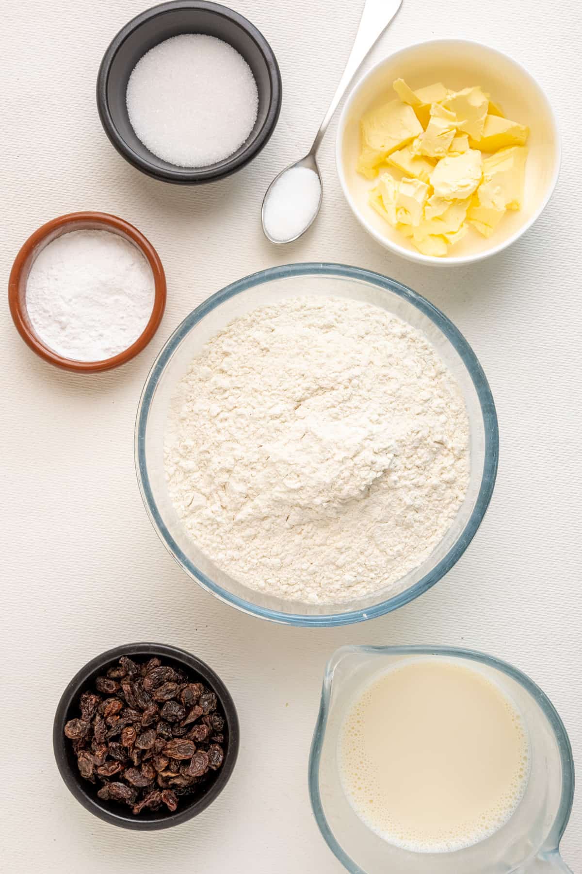 The ingredients for vegan scones. Plain flour, soy milk, vegan butter or margarine, sugar, baking powder, salt and raisins.