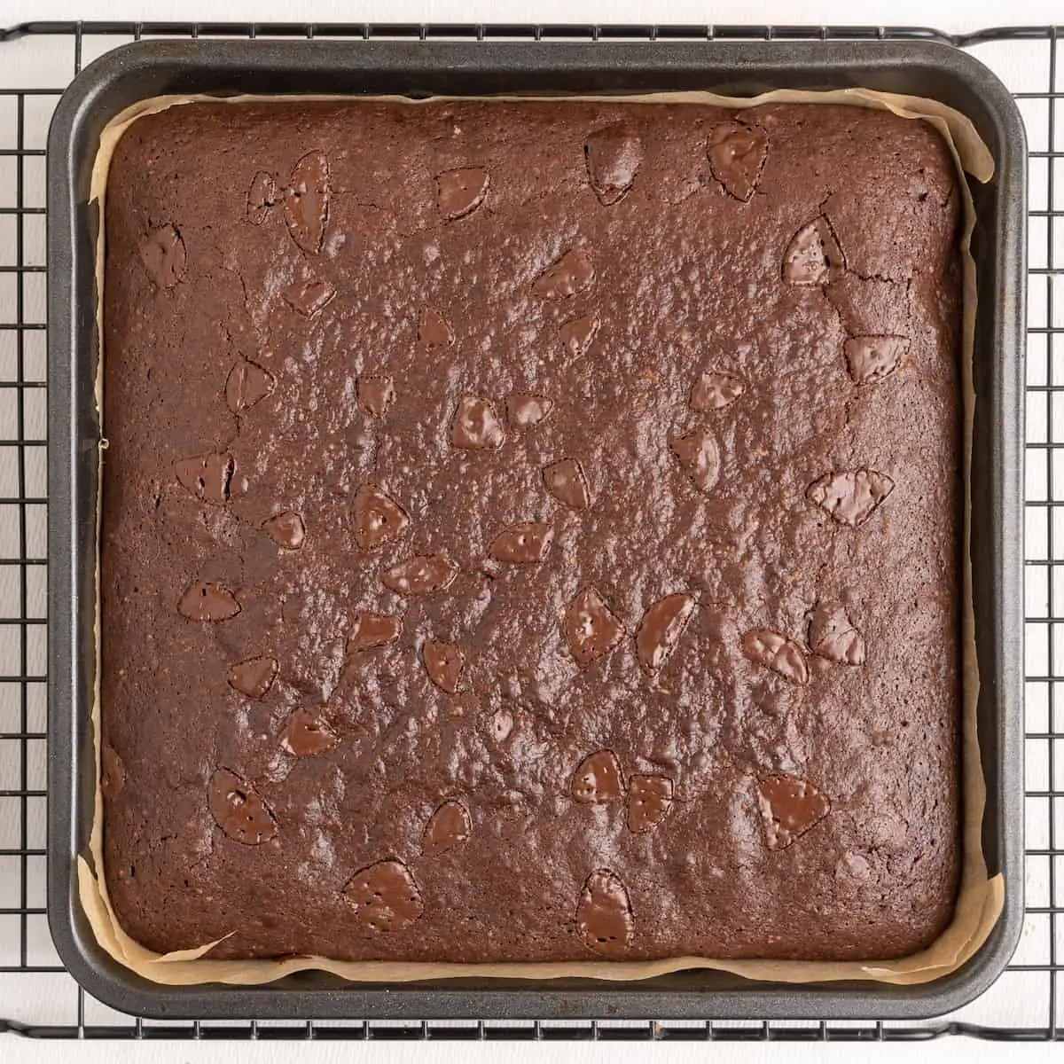The baked brownie in a tin on a wire cooling rack.