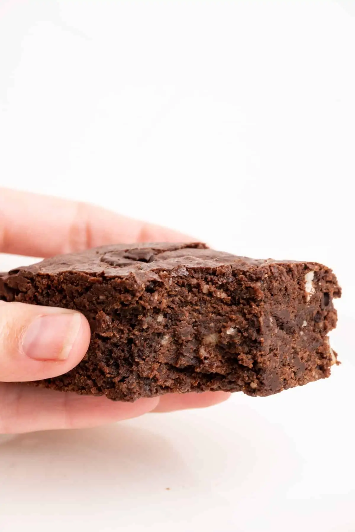 A hand holds a piece of brownie with a bite out of it.