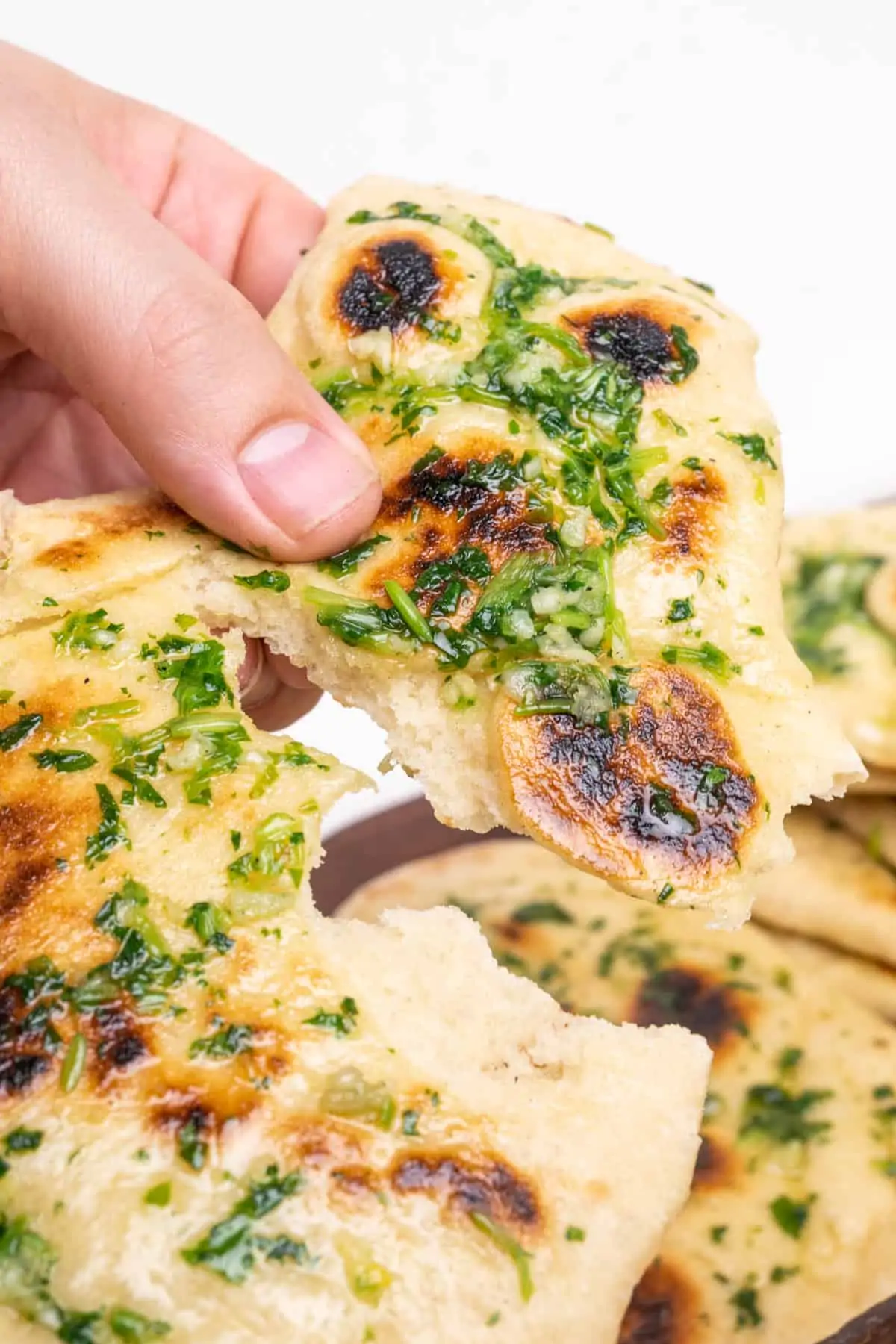A piece of naan bread being torn in two. The image illustrates the soft and light texture and the air bubbles turned into dark charred spots on the top of the bread.