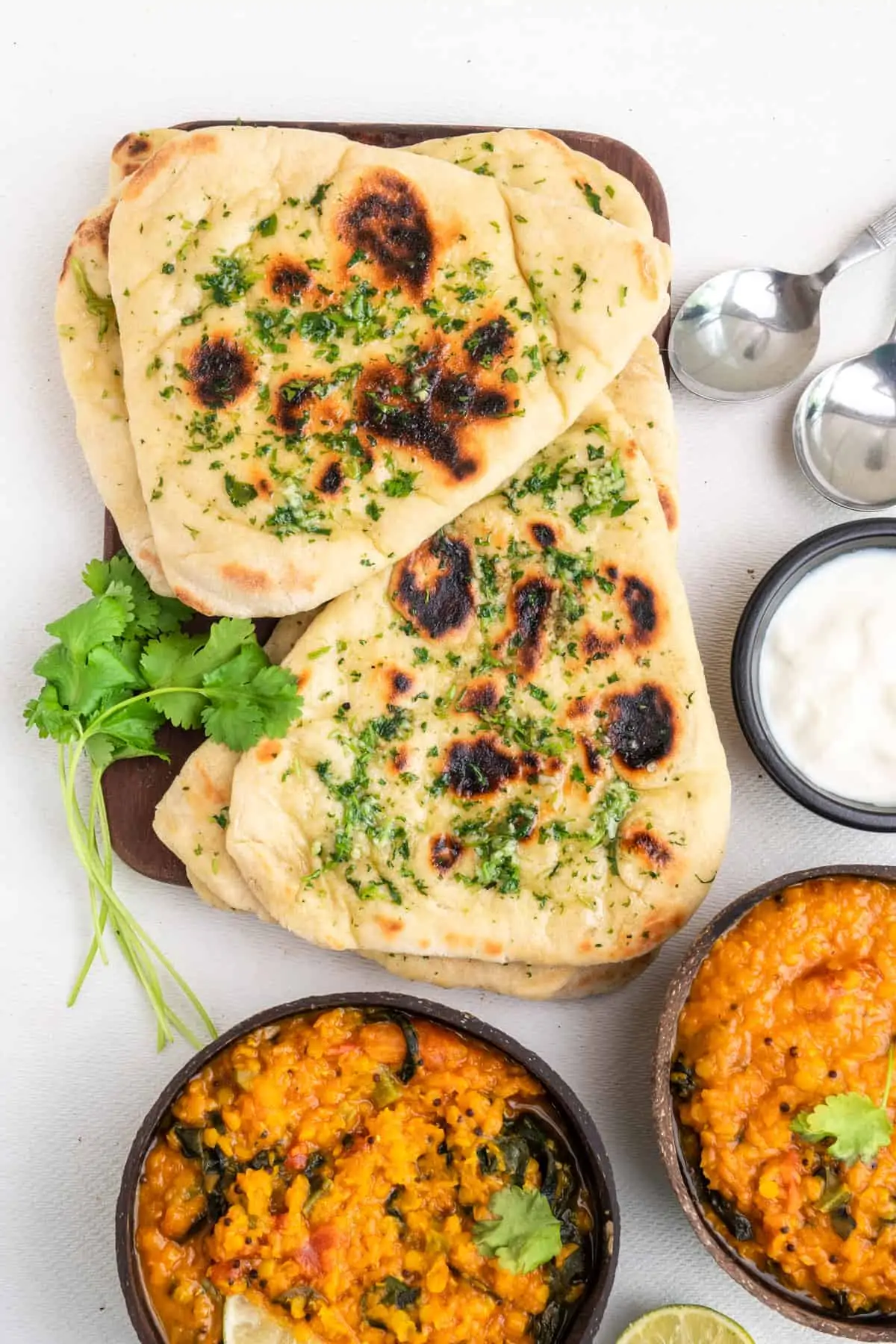 Garlic and coriander flatbreads in two stacks served on a dining table along with red lentil dal and yoghurt sauce.