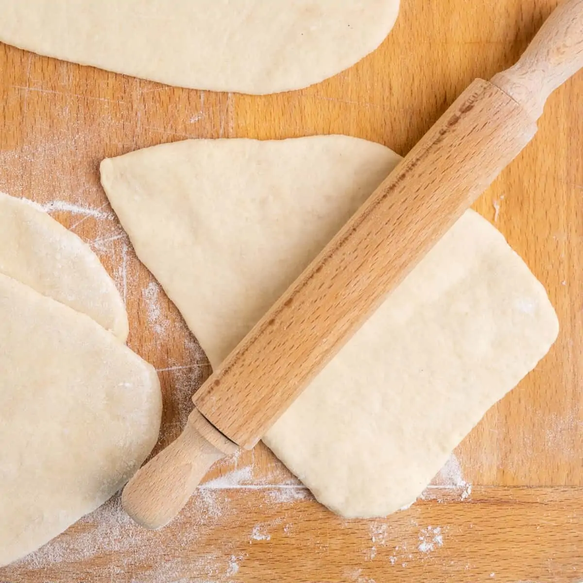 A piece of dough is rolled out flat with a rolling pin.