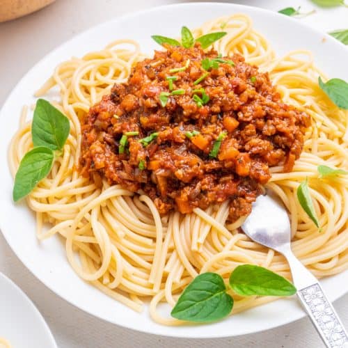 A plate of beautifully twisted spaghetti topped with a red bolognese sauce and garnished with chives fresh herbs.