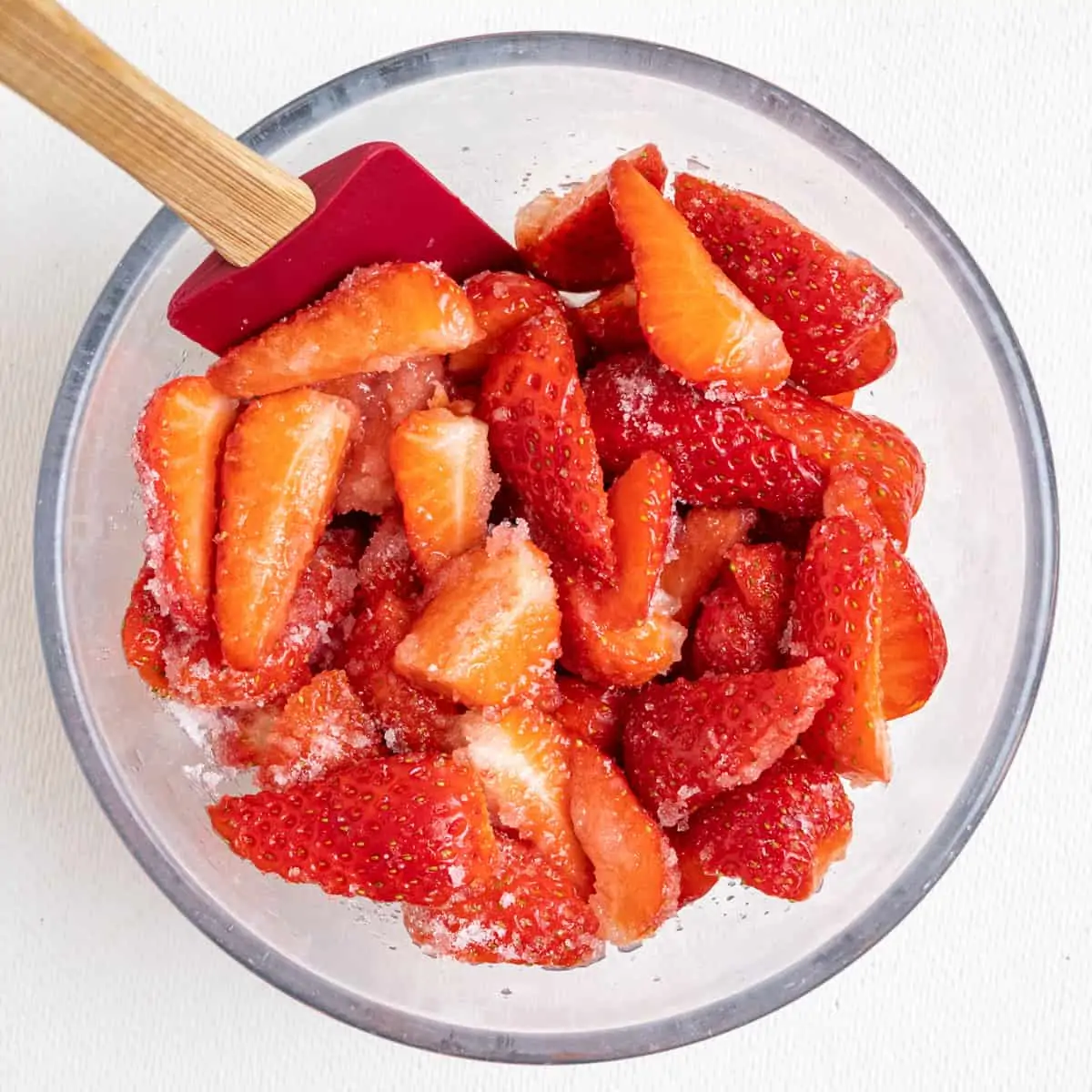 Quartered strawberries combined with granulated sugar in a glass bowl.