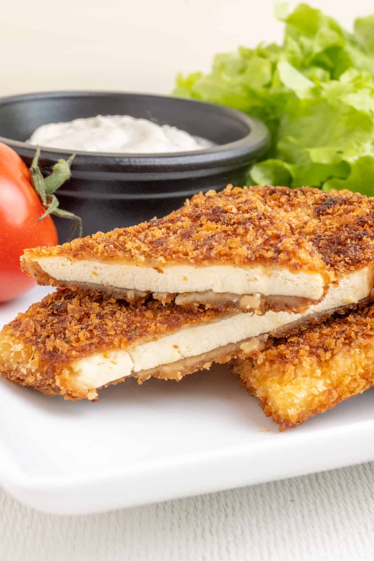The image depicts the crispy fried crust of golden brown breadcrumbs and the tender inside texture of a slice of breaded tofu cut in two.