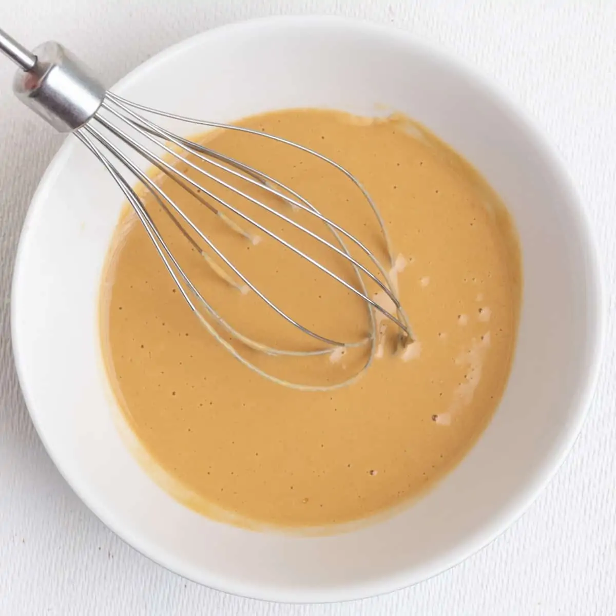 An light orange-brown batter and a whisk in a white bowl.