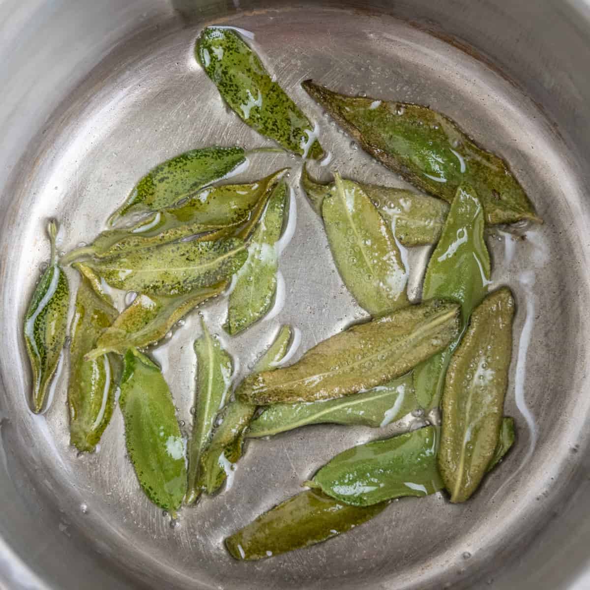A steel pan continging sage leaves frying in oil.