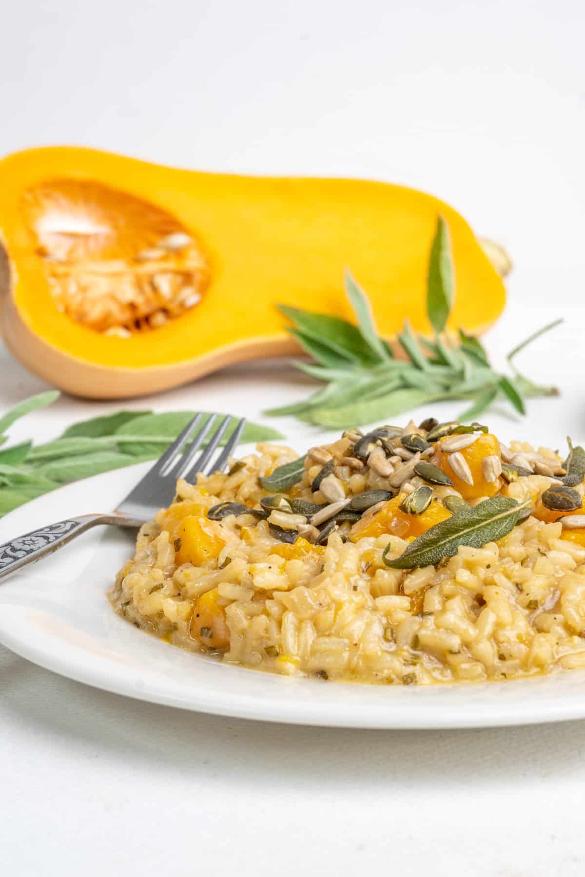 A plate of risotto with a fork. Half a butternut sqaush and sage leaves in the background.