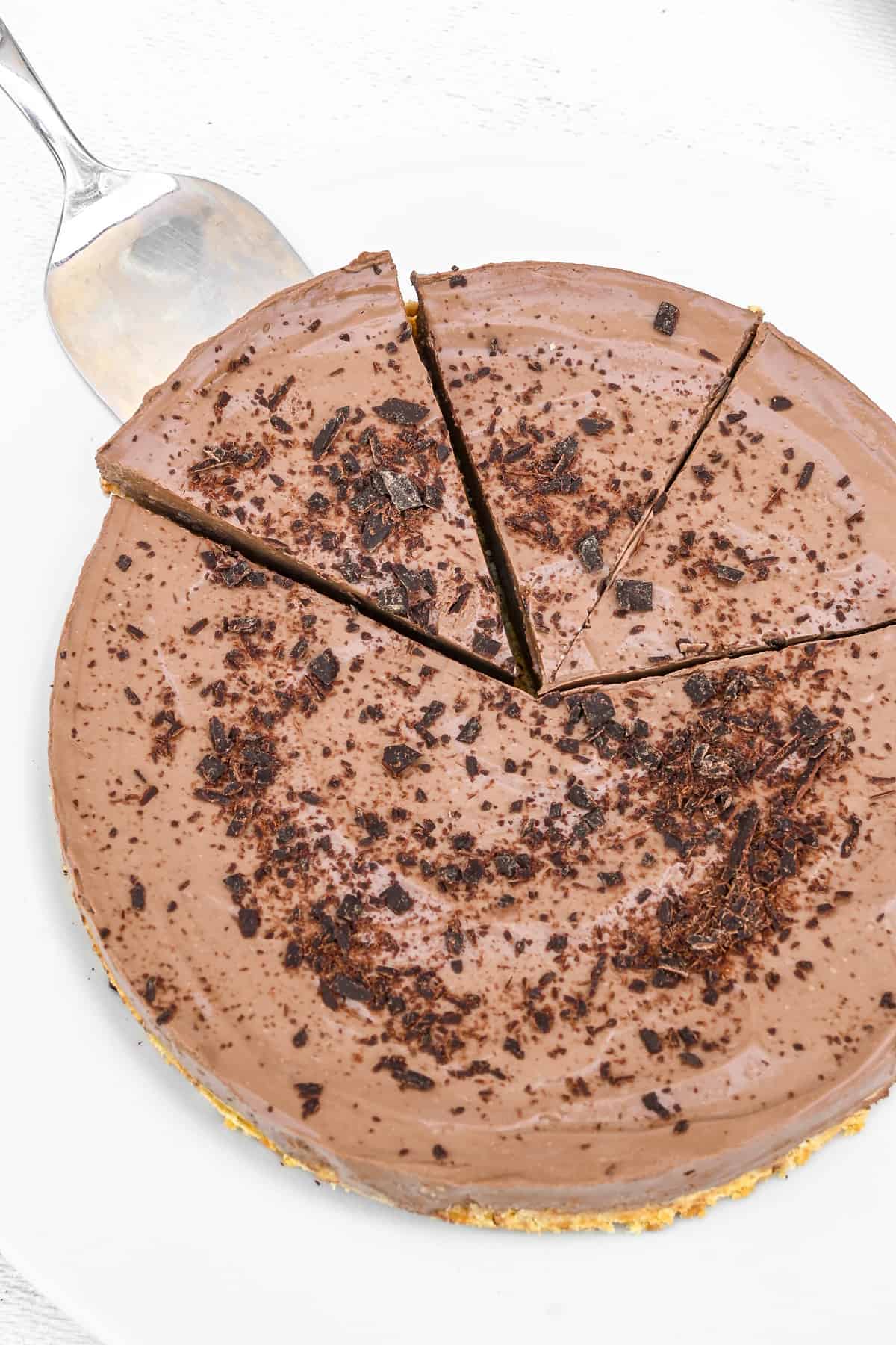 A top down shot of the tart, sprinkled with chocolate shavings. A slice is lifted away using a cake server.
