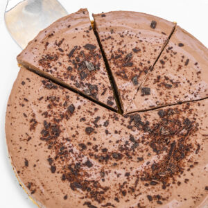 A top down shot of the tart, sprinkled with chocolate shavings. A slice is lifted away using a cake server.