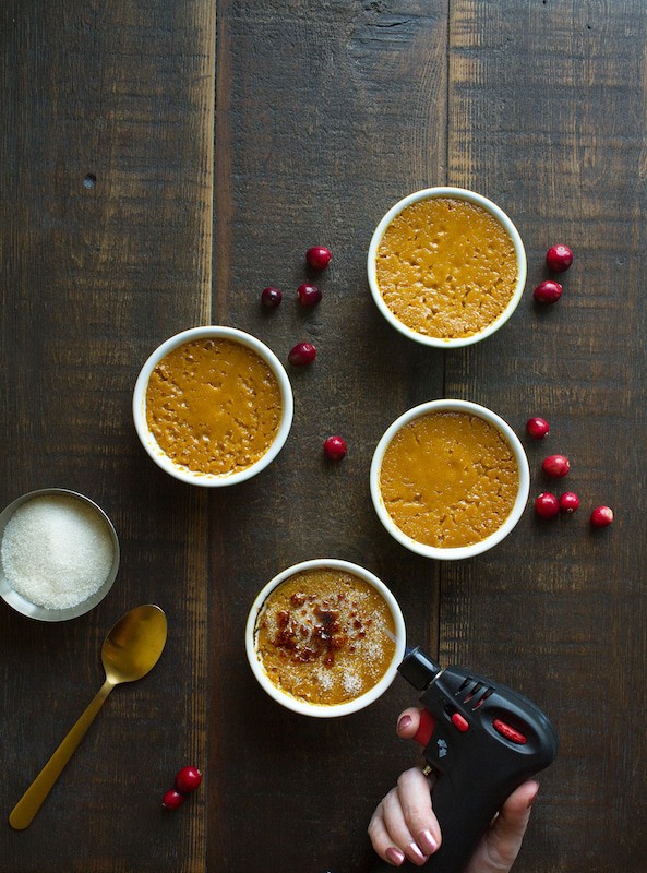 Four ramekins of pumpkin custard, one of which is having the brulee topping caramelised with a torch.