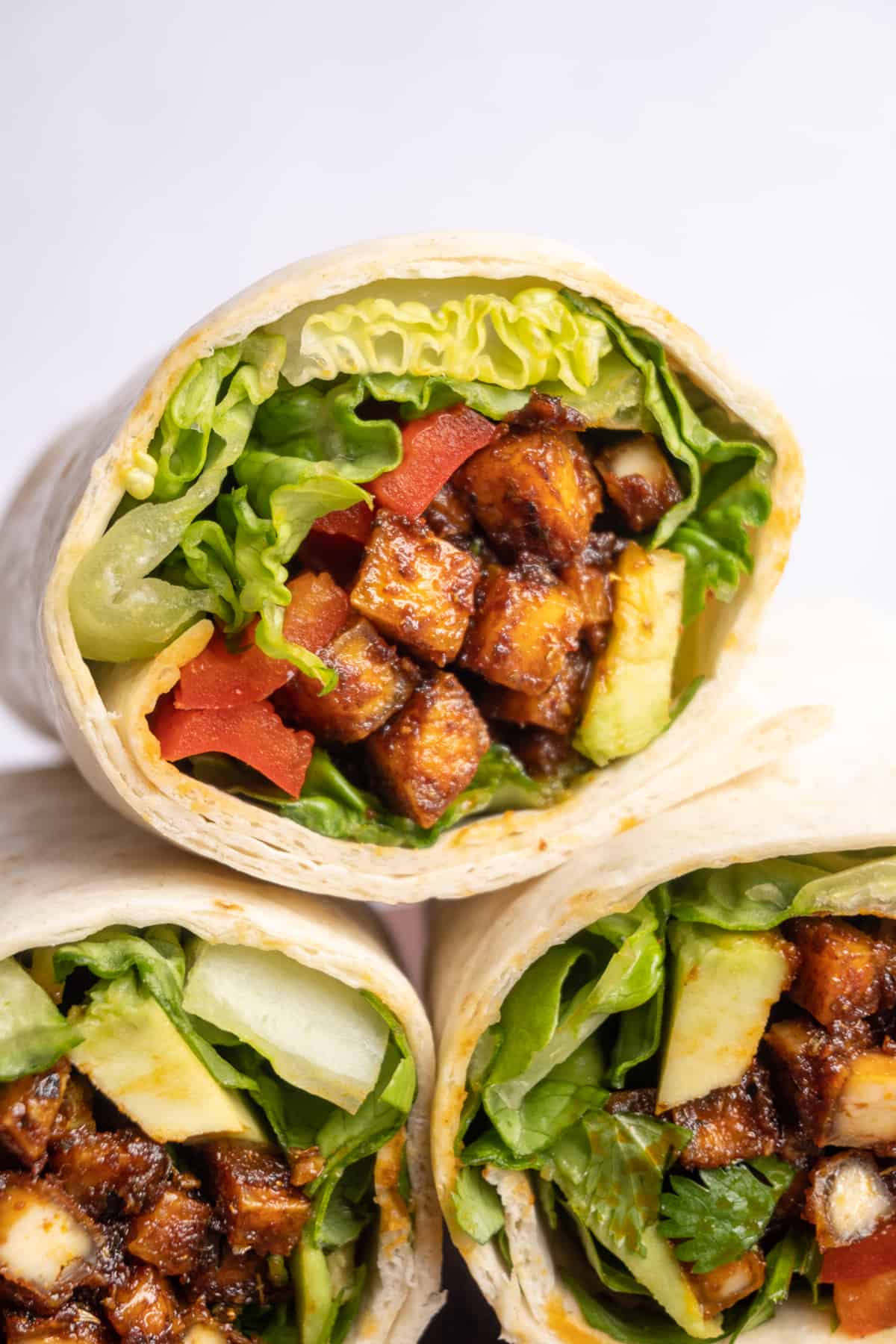 Tortilla wraps sliced in half, showing the filling of vegetables and spicy coated tofu cubes.
