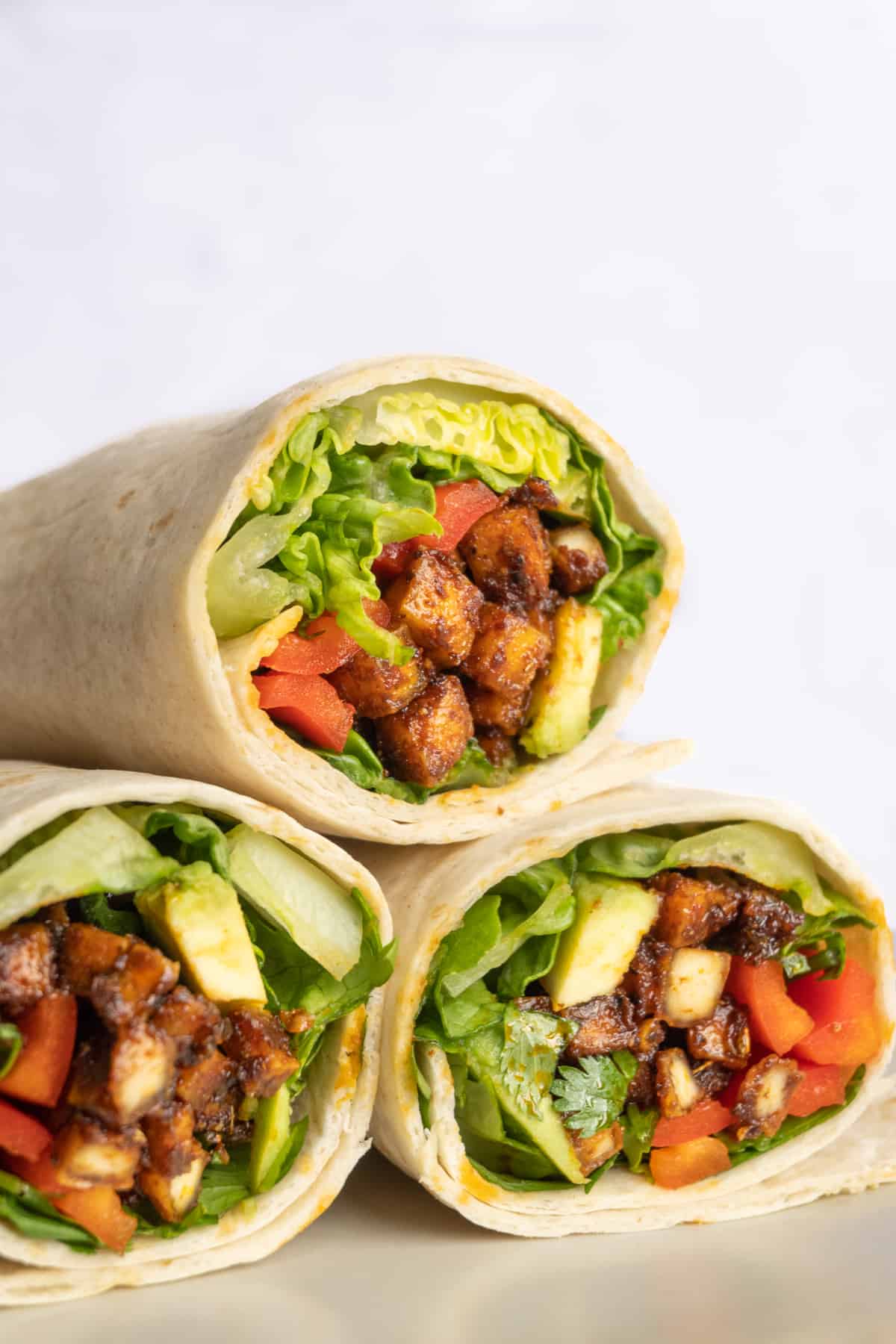 Tortilla wraps sliced in half, showing the filling of vegetables and spicy coated tofu cubes.