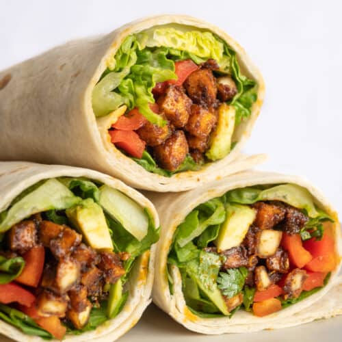 Tortilla wraps sliced in half, showing the filling of vegetables and spicy coated tofu cubes.