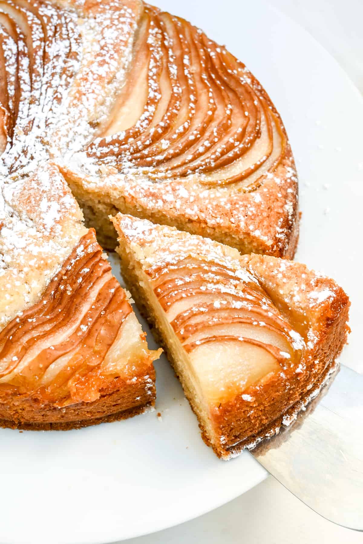 A slice is cut from the round pear cake and lifted away.