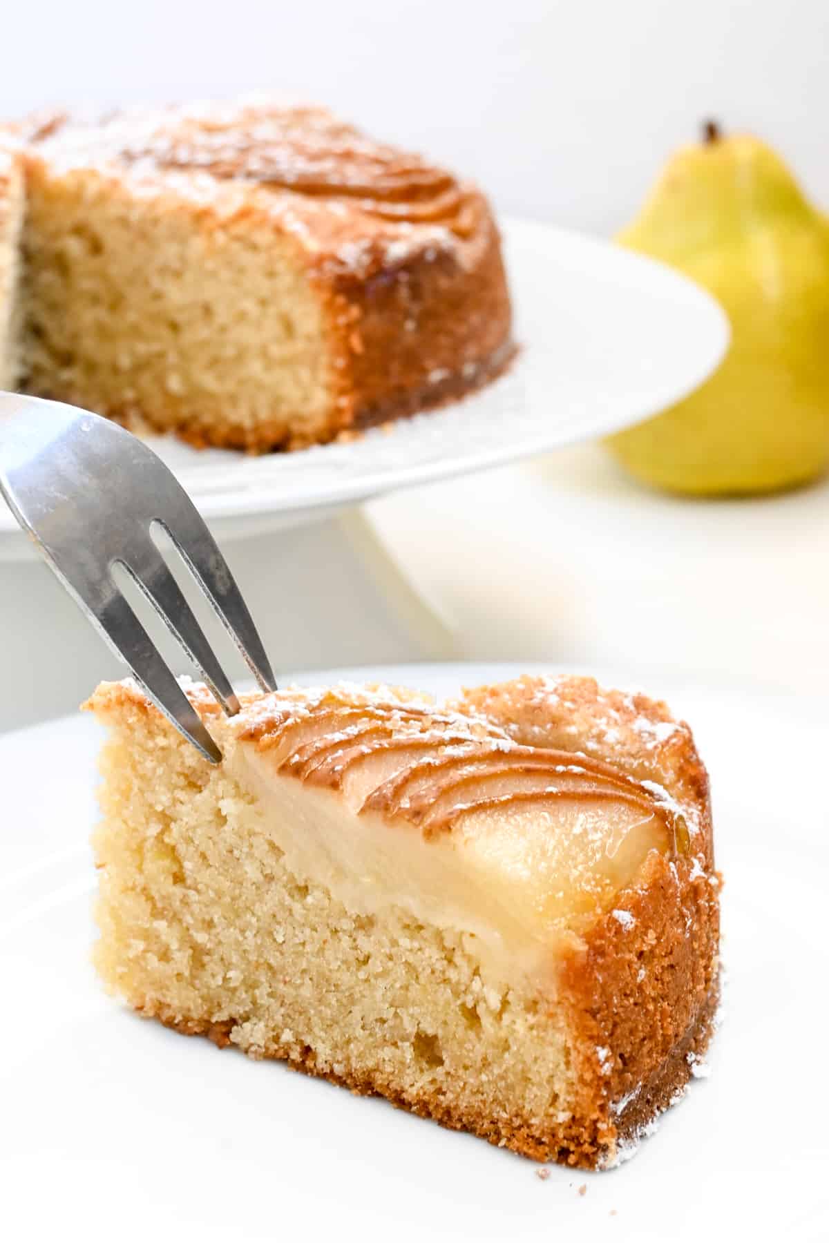 A fork cutting into a slice of cake with slices of pear arranged on top.