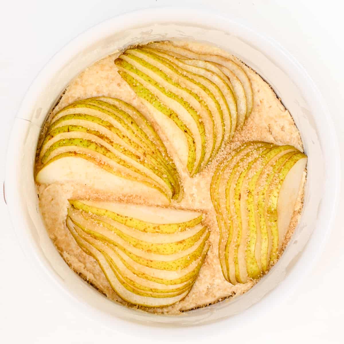 Slices of pears artfully arranged on top of the batter in a small springform tin.