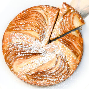 A slice is cut from the round pear cake and lifted away.