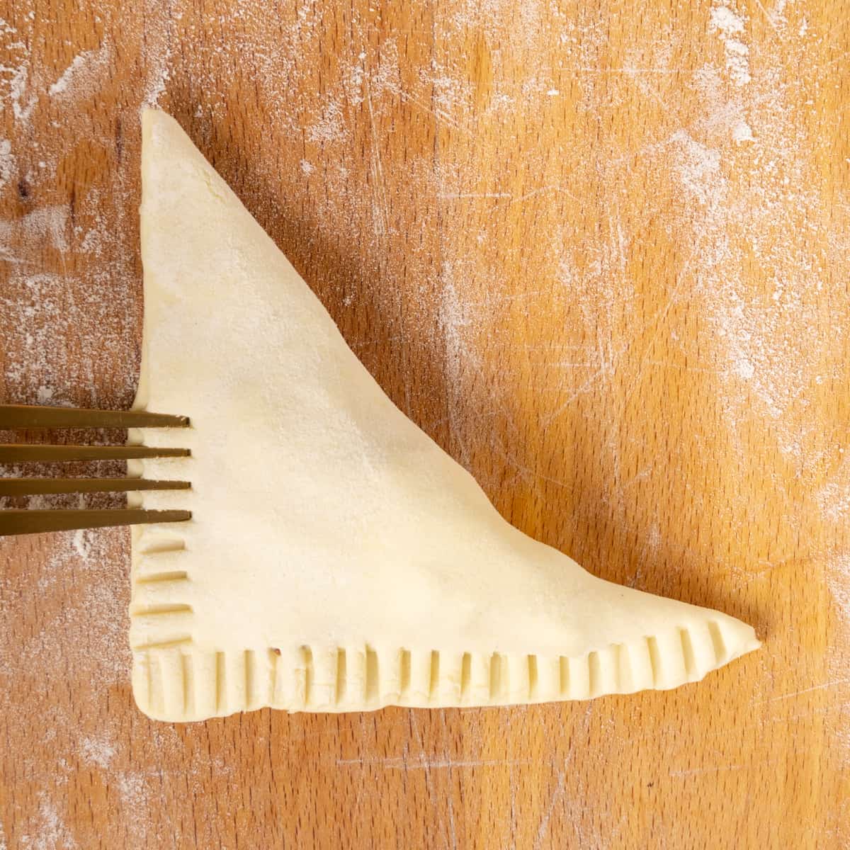 Crimping the edges of the turnovers with a fork to seal them tightly.