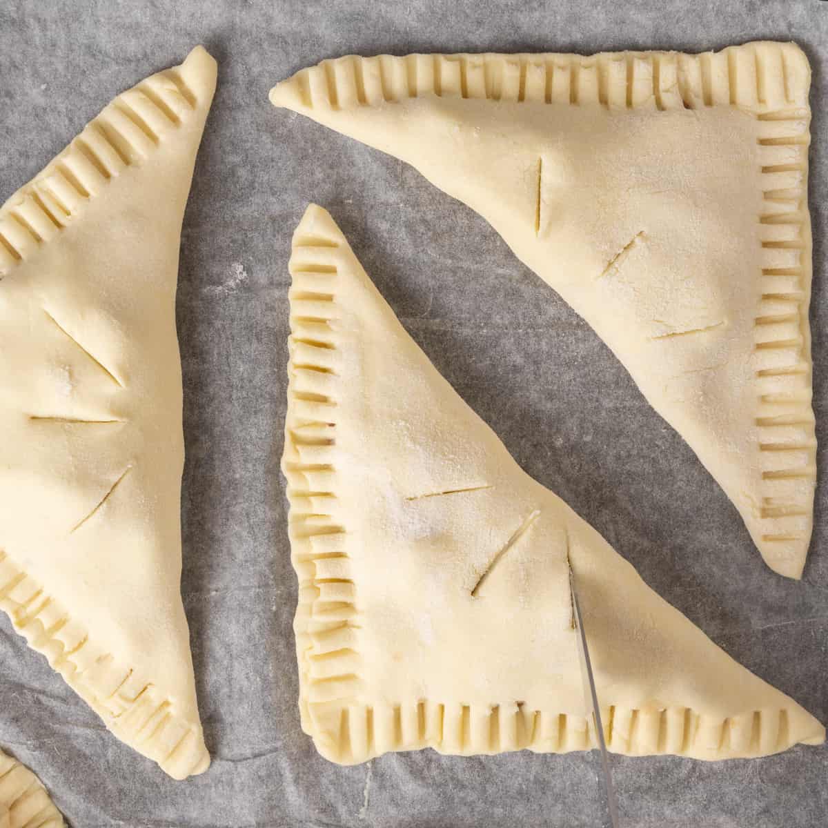 A knife cutting slits into the top of the triangular puff pastry pockets.